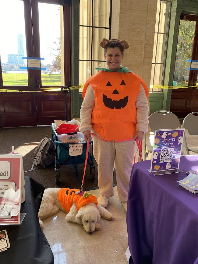 person dressed in pumpkin suit with a poodle also dressed in a pumpkin suit