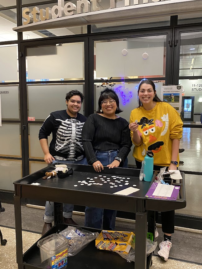three people standing in halloween costuming in front of a trolley with candy on top