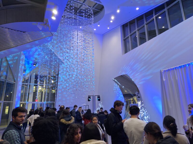 A photo inside the Stata center with a hanging light display and a line of people waiting for a dessert buffet.
