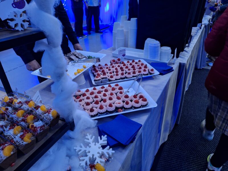 Mini chocolate cupcakes with pink frosting on a long white table with fake snow and snowflake decorations