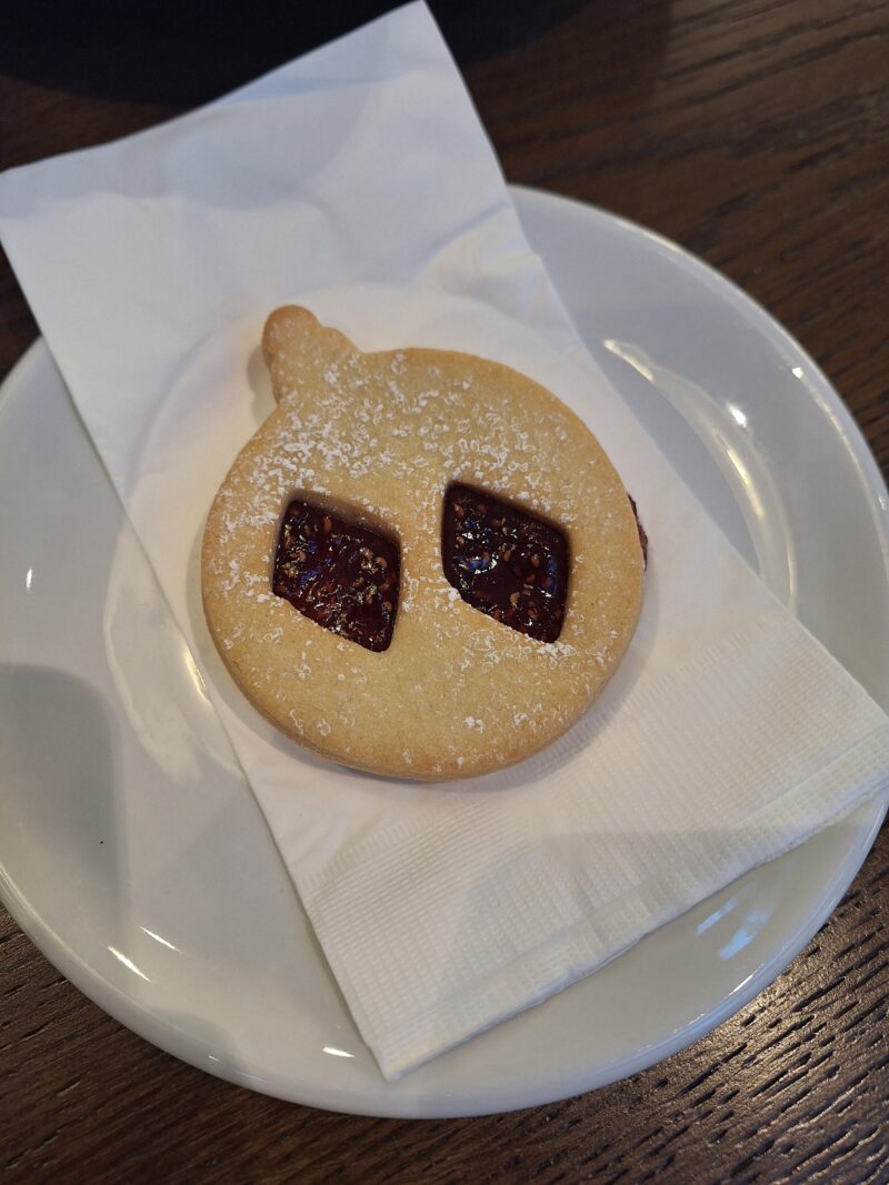 A linzer cookie in the shape of an ornament with two slits exposing the red jam in the middle on a plate with a napkin.