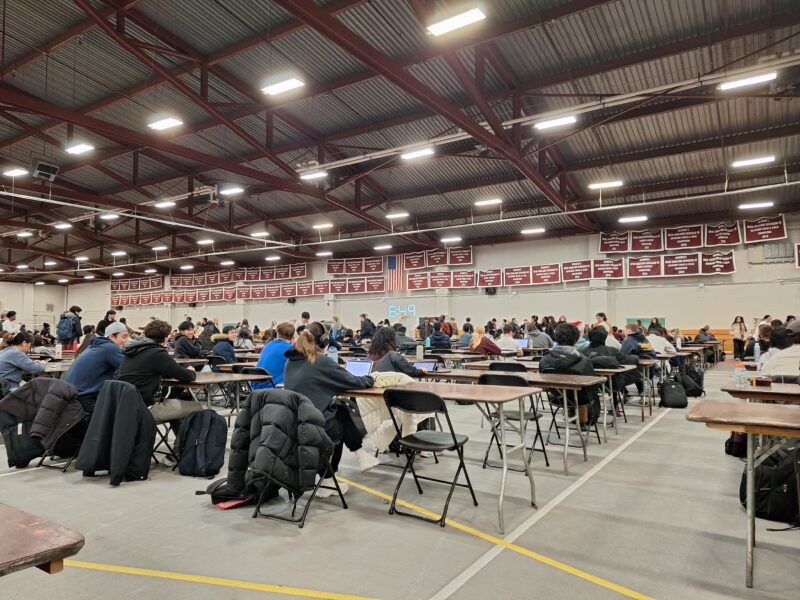 A large gymnasium with hundreds of students taking an exam.