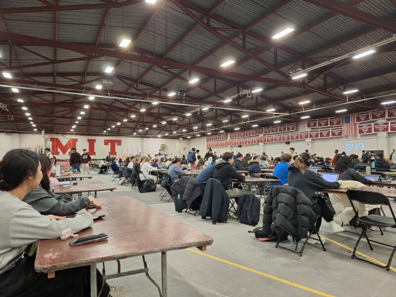 A large gymnasium with hundreds of students taking an exam.