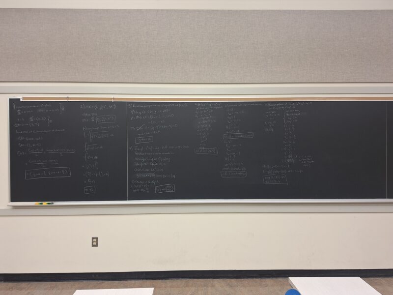 A wall-length blackboard with practice problems for multivariable calculus.