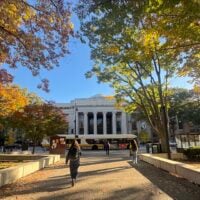 Photo of MIT building 7 surrounded by trees changing color against a clear blue sky.