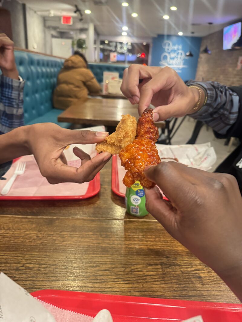 Photo of three people hold chicken wings together in a