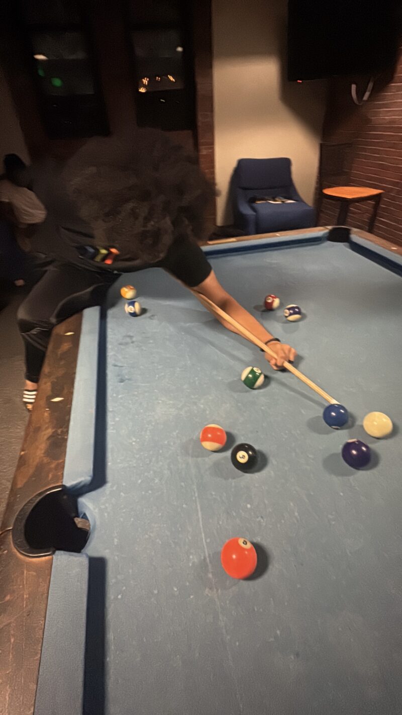 Another photo of student putting pool stick behind their back to attempt a trick shot.