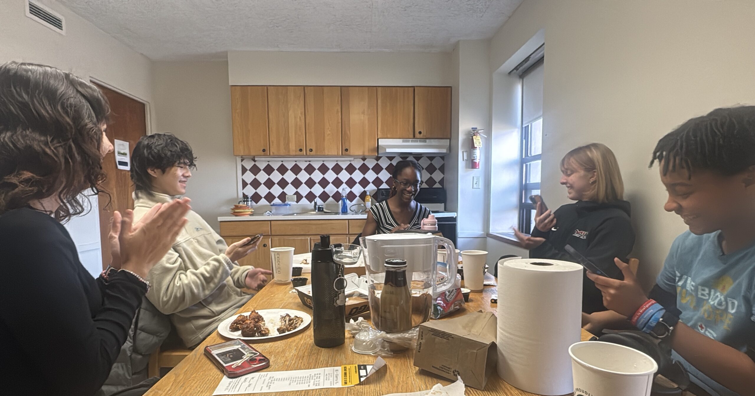 Group photo of students at table enjoy wings and checking their final physics grade.