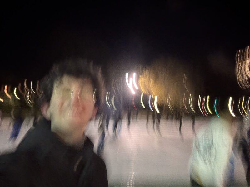 A blurry selfie of a guy on the outskirts of an ice skating rink.