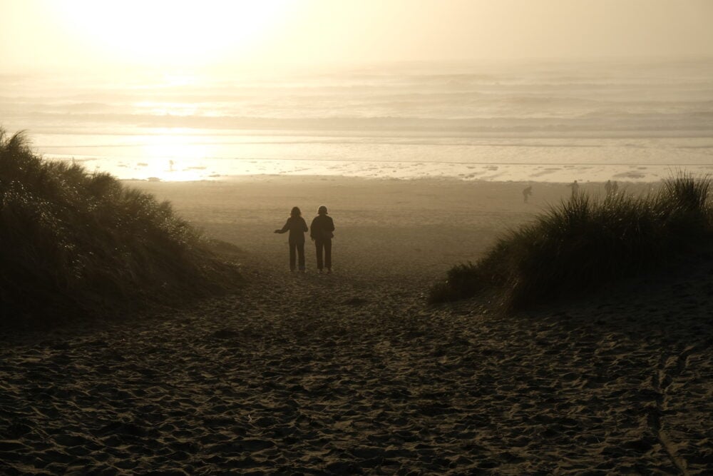 silhouette of two people on a beach, walking towards the sunset and the ocean