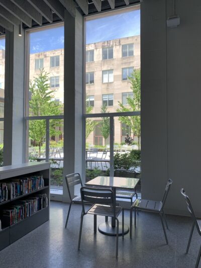 a corner of a library with large windows looking out to a courtyard with trees