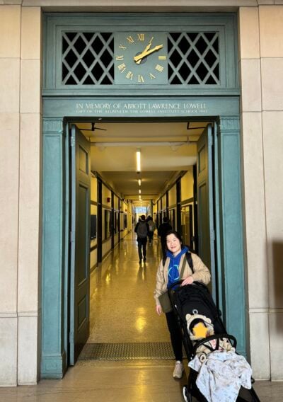 Woman and baby in a stroller in front of a long hallway.