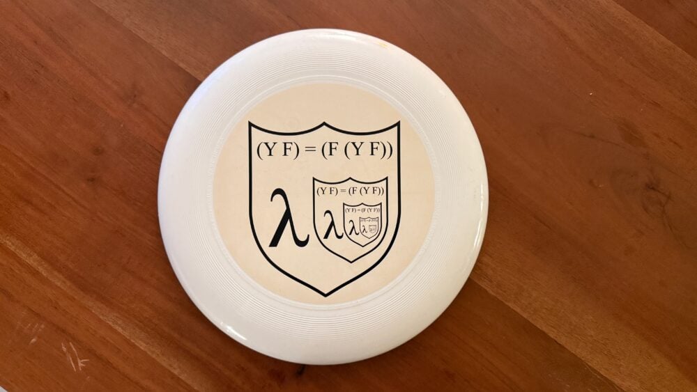 A white frisbee featuring the MIT Scheme logo, a coat-of-arms with the equation of the fixed-point combinator and a smaller recursive MIT Scheme logo.