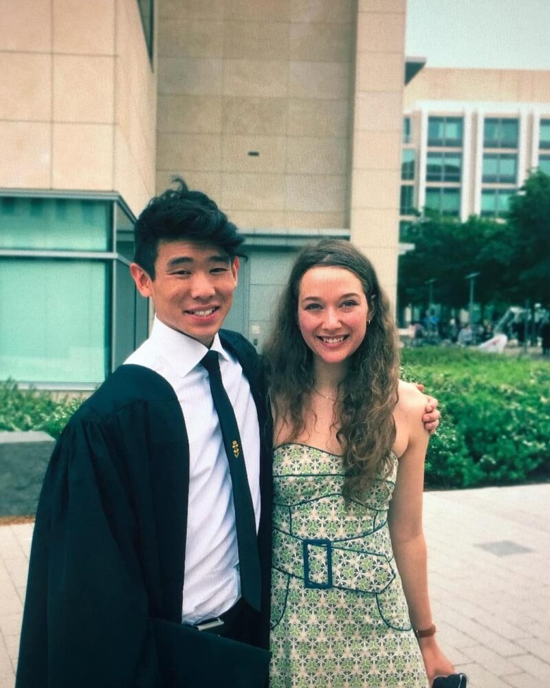 A young white woman with long brown hair in a green dress and young Chinese man in a white shirt, tie, and black graduation gown.