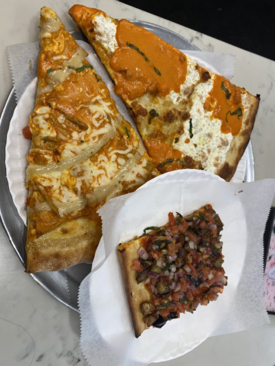 A metal tray holding three slices of pizza, two topped with creamy orange sauce and one topped with diced vegetables and herbs.