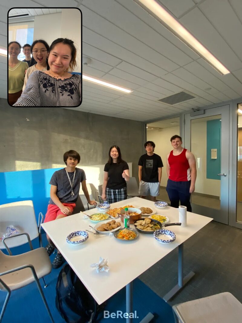 photo with people standing on two sides and there is food on the table