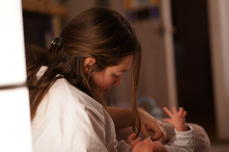 a woman with light brown hair viewed from the side looking down at a small baby in her arms