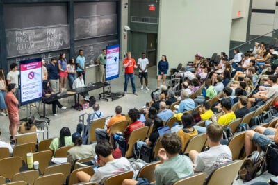 Man presenting to audience with a poster beside him.