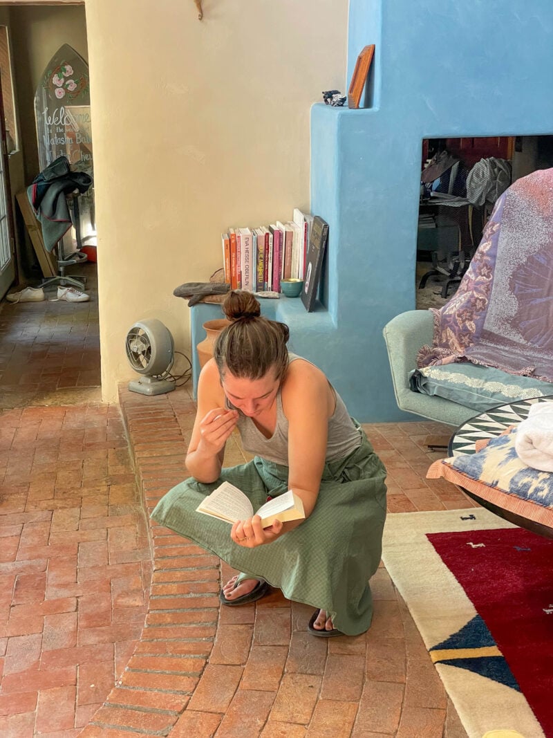 the author squatting in the middle of a colorful room, reading a book