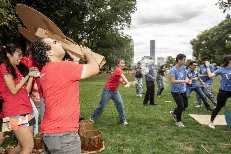 Woman throwing water balloon on a grass field at other people.