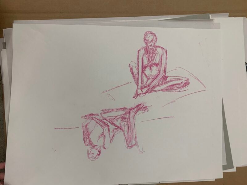 The image features two sketches rendered in pink crayon on white paper. The first figure, oriented upright, is depicted in a sitting position with legs drawn up, showcasing minimal detail but clear anatomical shapes. The second figure, positioned below and inverted, presents a relaxed pose with limbs extended outwards. The paper has a clean, white background, while the sketches are centered, without borders or framing elements, emphasizing the figures on the stacked sheets of paper.