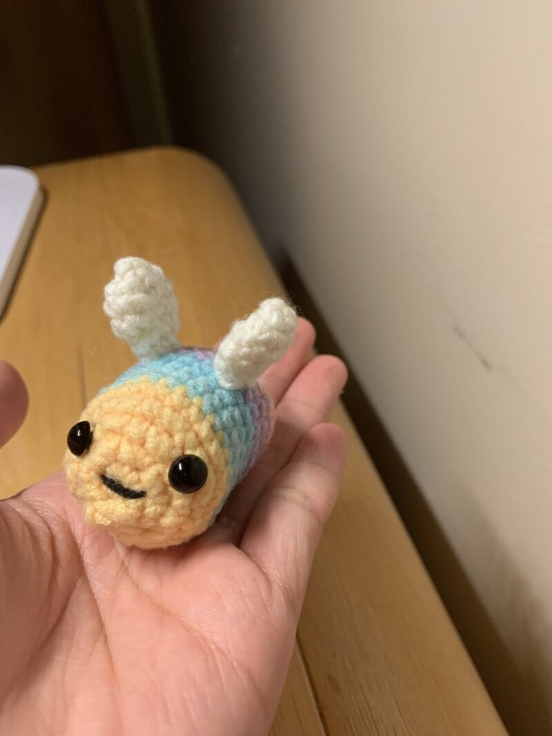 A charming small crocheted toy with a smiling face, emphasizing its unique craftsmanship and playful appearance.