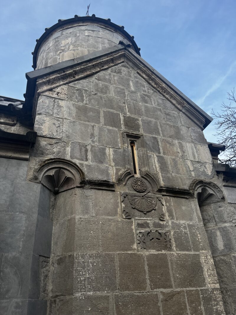 Close-up of an Ornate Armenian Church Wall – A detailed view of a medieval Armenian church’s stone wall, featuring delicate carvings, an arched window, and historical inscriptions.
