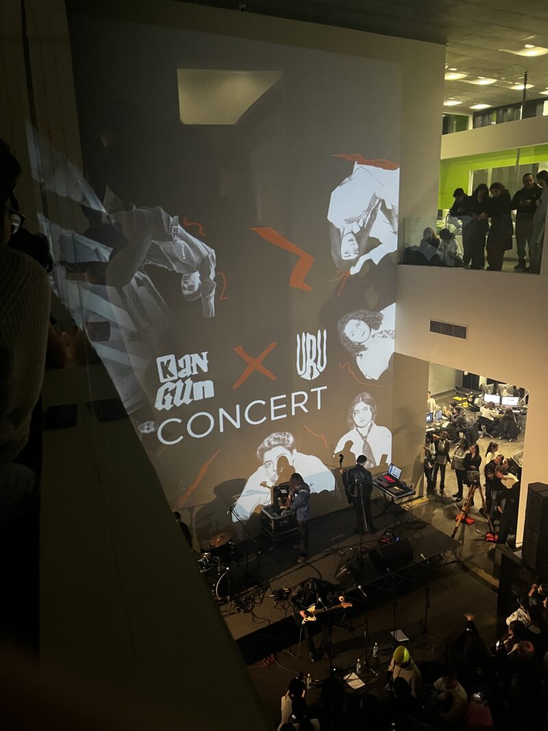 Live Concert Projection on a Wall – A concert venue features a large projected display of the artists performing, with musicians playing instruments on stage and an audience gathered around.