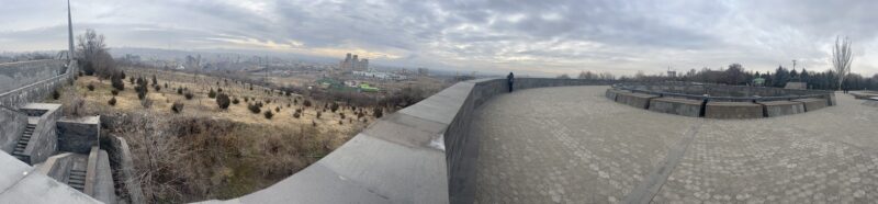 Panoramic View of Yerevan from a Memorial Site – A wide-angle view of Yerevan, Armenia, from an elevated memorial site. The cityscape stretches into the distance, with patches of trees and a monument in the foreground.