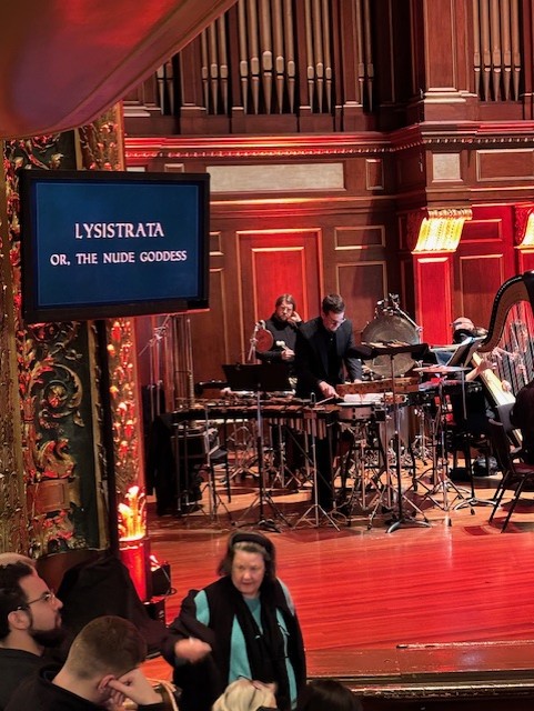 wider show showing stage and two percussists, both behidn a ton of instruments. One of which is a metalic xylophone, called a glockenspiel.