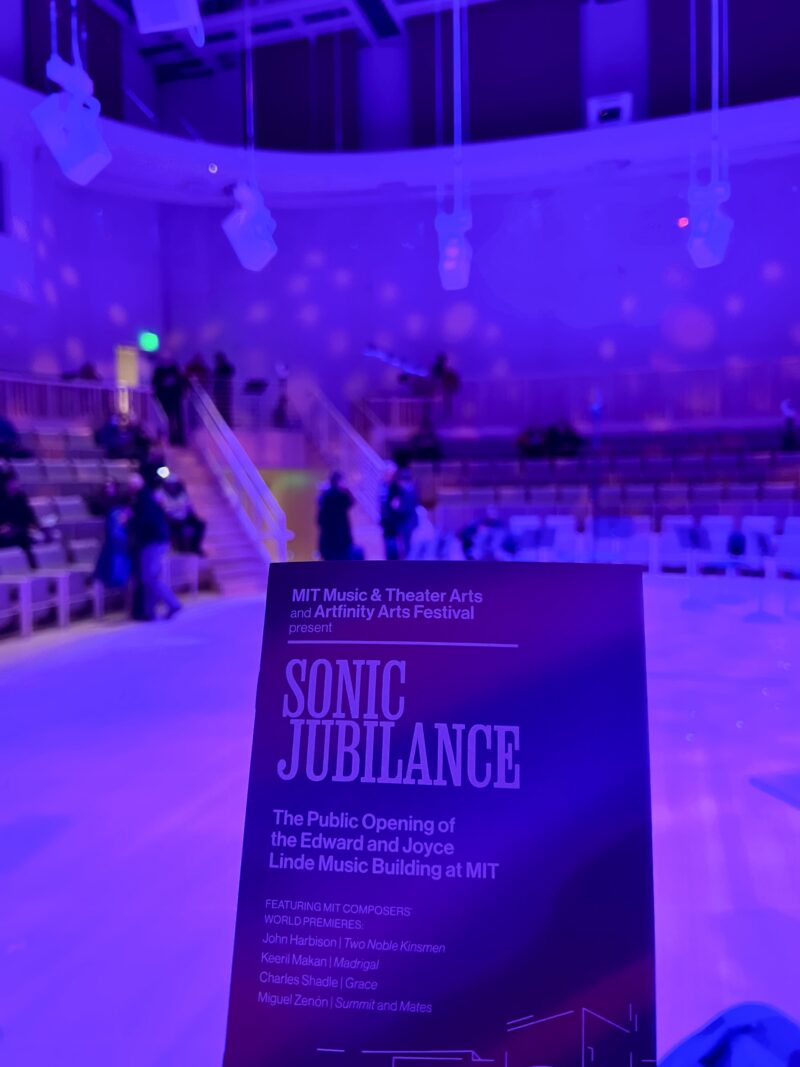 Program for the Sonic Jubilance concert, with the Thomas Tull Concert Hall in the background, lit up in purple lights.