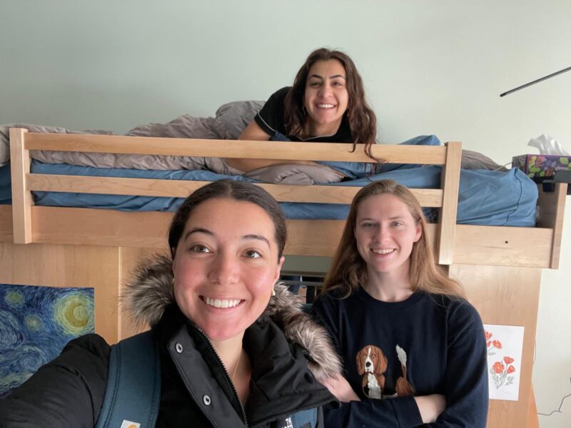Three people smiling for a selfie in a dorm room.