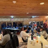 Long tables in a wooden cabin with students working on their computers.