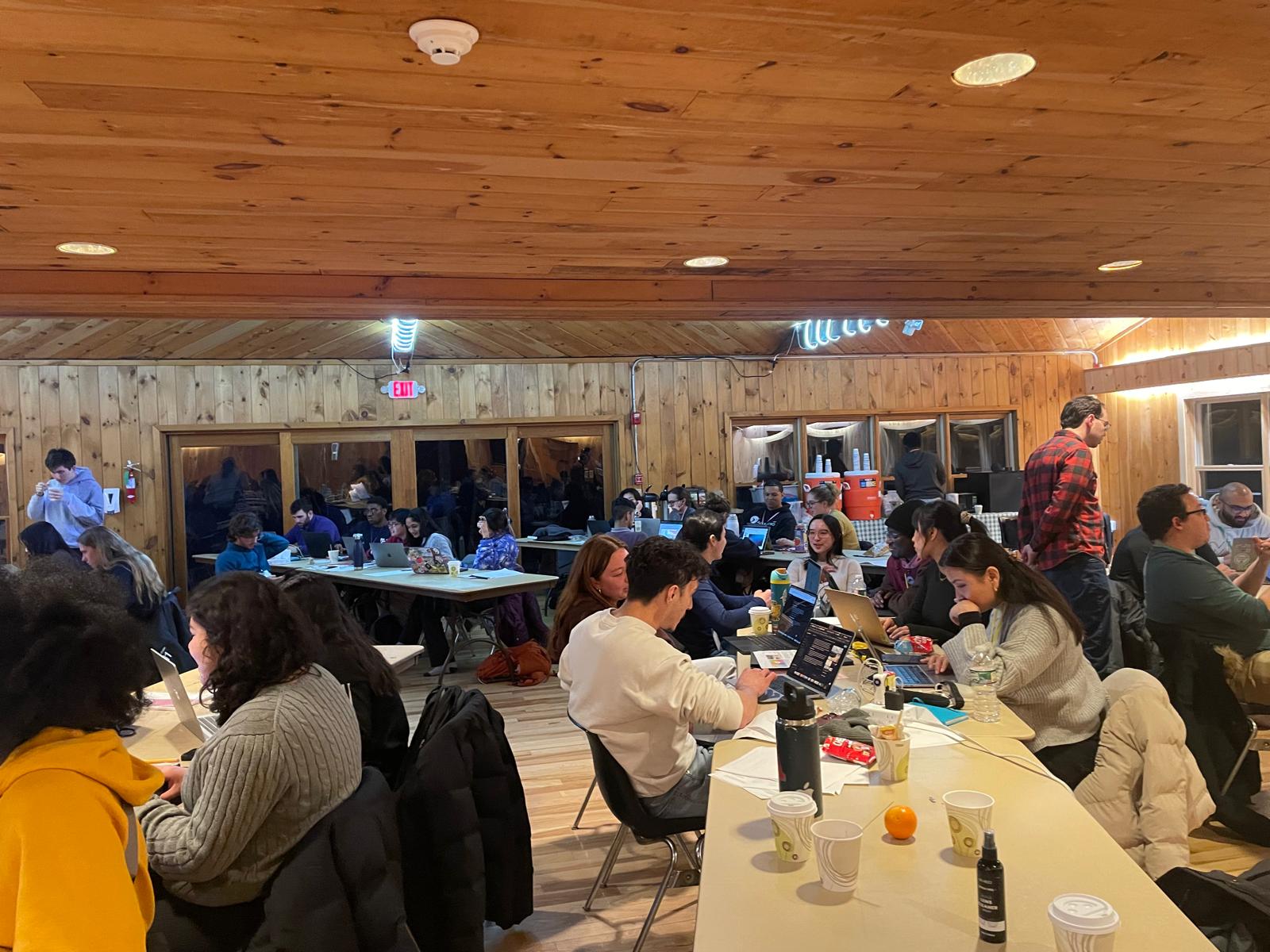 Long tables in a wooden cabin with students working on their computers.