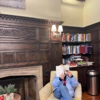 Girl reading a book in an armchair with books behind her.