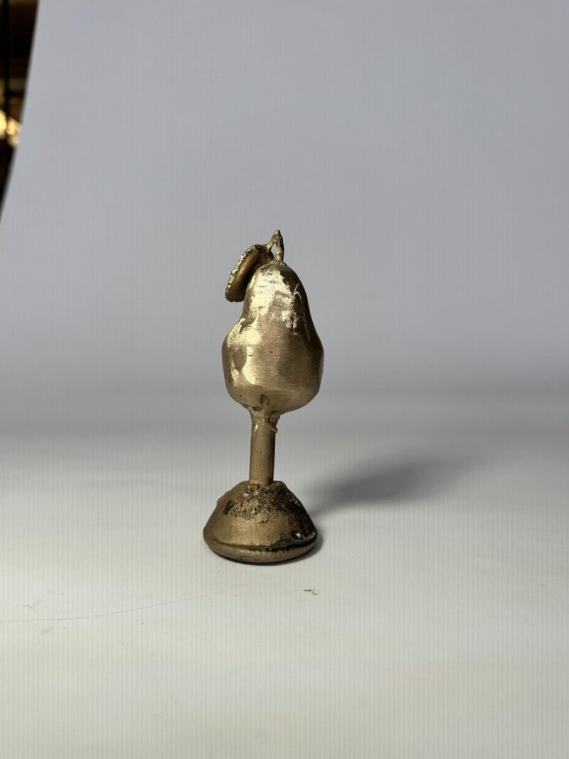 A beautifully crafted gold pear sculpture resting on a stand, emphasizing its shiny surface and artistic elegance.