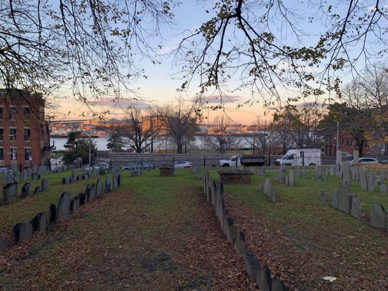 Sunset view from a cemetery overlooking a river, with scattered grave markers and trees in the foreground.