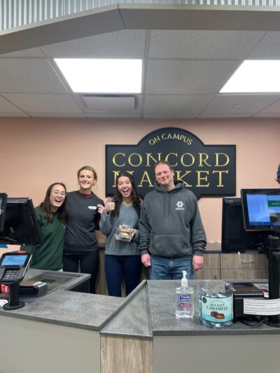 Four people posing behind a grocery store register with Concord Market in the background.