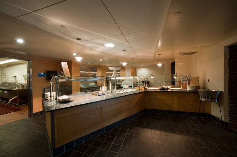 The entrance to a dining hall with a long wood counter going across. The lighting is dark and no food is set out.
