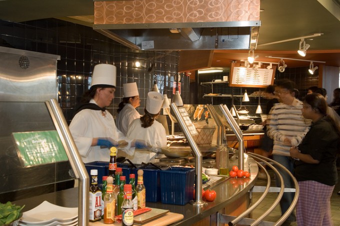 The side view of a round grill station with two workers preparing stir fry.
