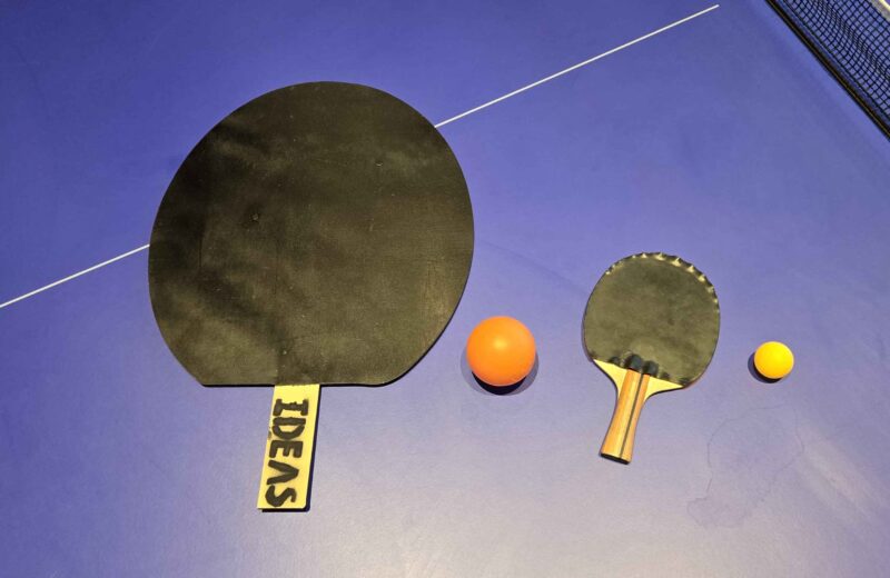 two pairs of ping pong paddles and balls, one about a twice as big as the other
