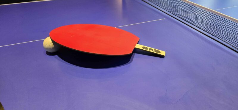 large ping pong paddle resting on large ping pong ball