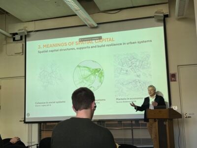 a picture of someone gesturing at a presentation slide with several map diagrams on it