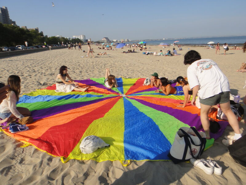 people on the beach sitting on a rainbow parachute