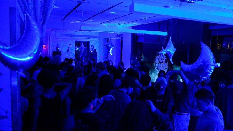 A blue-lit room with a crowd of people dancing.