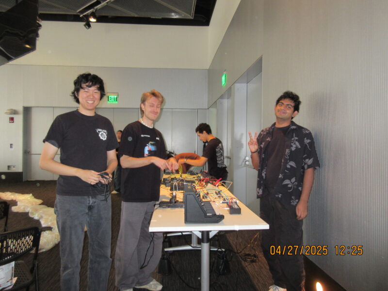 some people standing around a table with a bunch of synths and wires on it