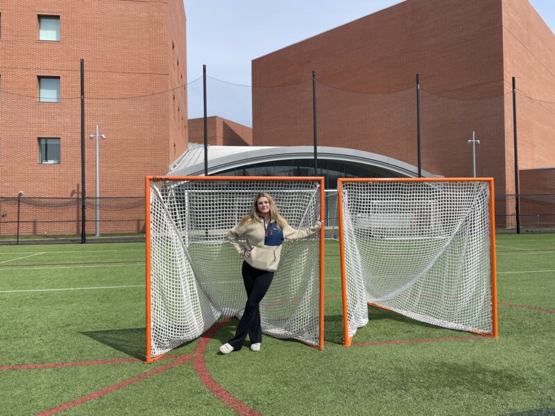 Girl posing inside a lacrosse goal.