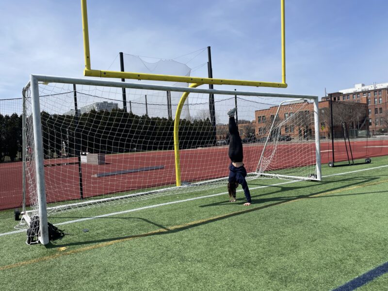 Girl doing handstand in front of goal and football posts.