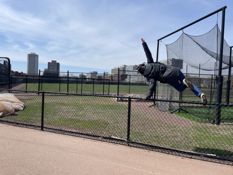 Girl jumping over fence with arm and leg out.