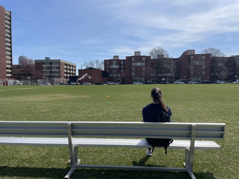 Girl sitting on bench overlooking grass field.